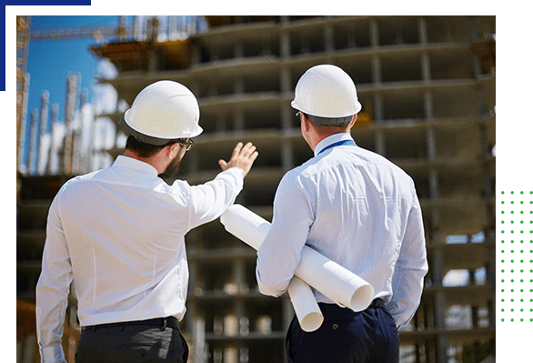 Two men in hard hats and white shirts are looking at a building.